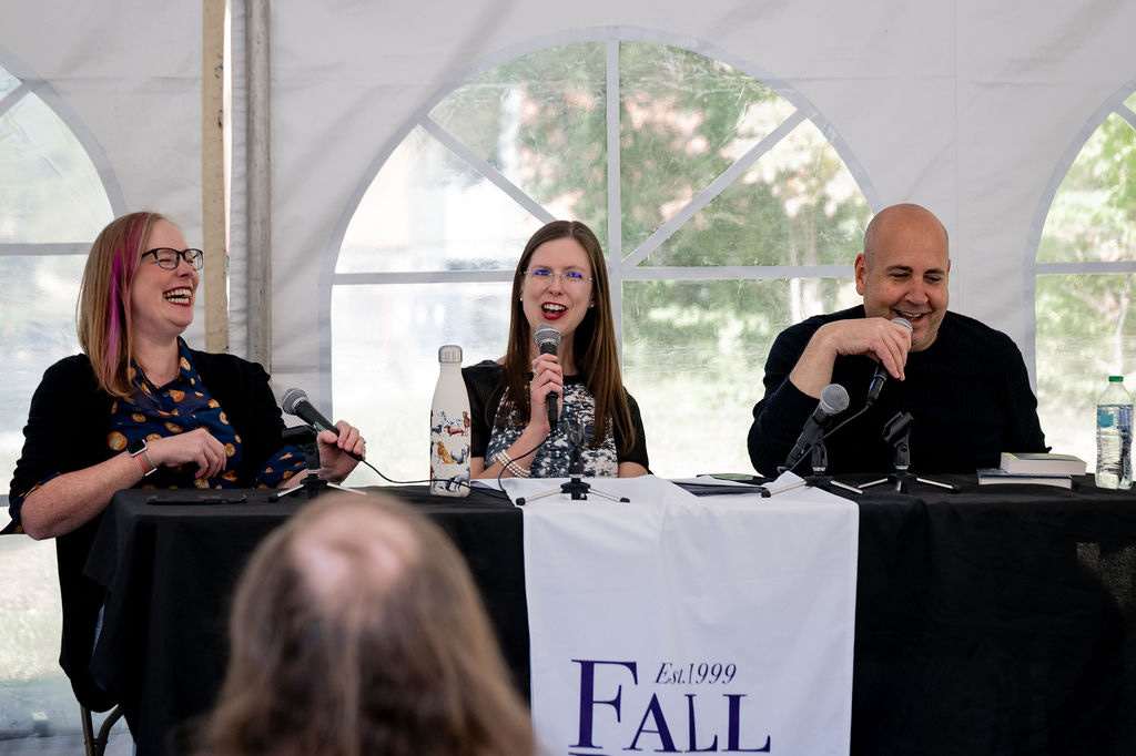 Catherine Olien speaking into a microphone between two laughing panelists at a Fall for the Book event