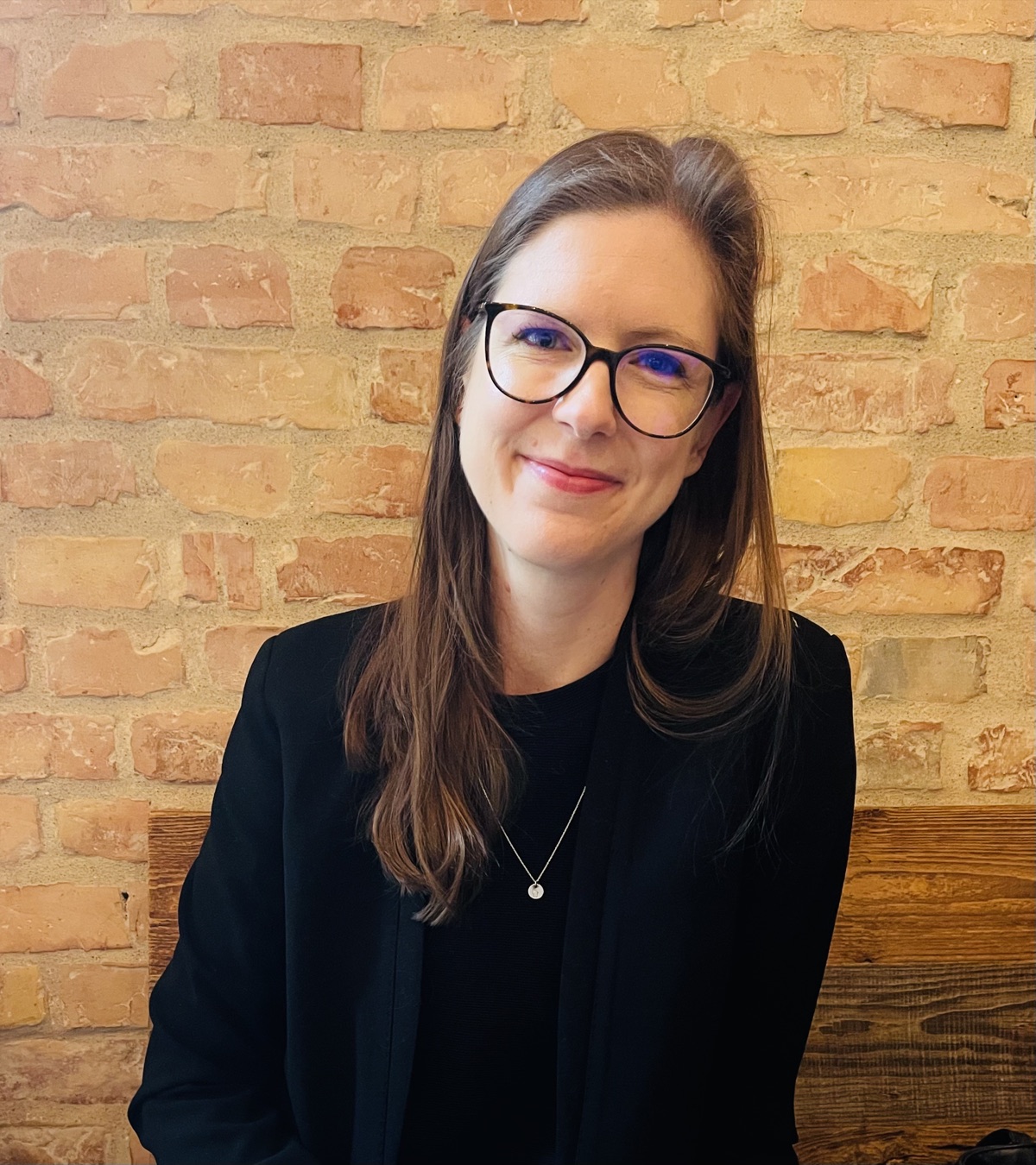 Catherine Olien in a black blazer, smiling, against a brick wall